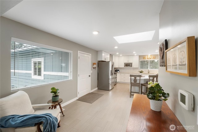 kitchen featuring plenty of natural light, white cabinets, a skylight, and stainless steel fridge with ice dispenser