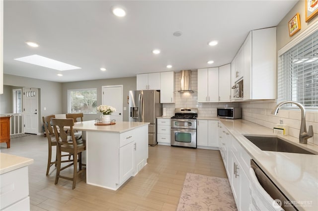 kitchen with a kitchen bar, a skylight, stainless steel appliances, wall chimney exhaust hood, and a sink