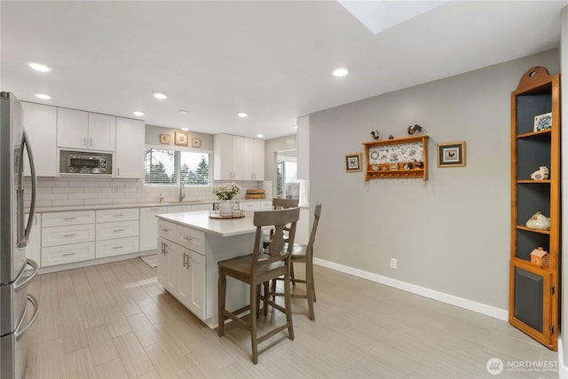 kitchen featuring backsplash, a kitchen bar, light countertops, freestanding refrigerator, and white cabinets