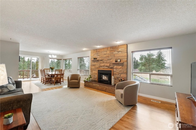 living room featuring visible vents, baseboards, a stone fireplace, wood finished floors, and a textured ceiling