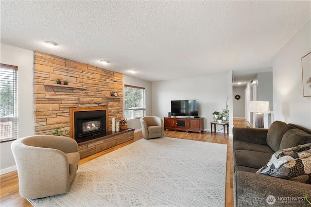 living area with a stone fireplace, plenty of natural light, and wood finished floors