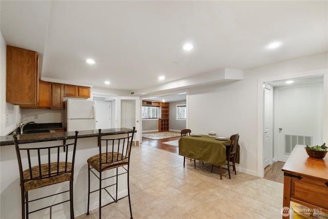 kitchen featuring visible vents, a breakfast bar, a peninsula, freestanding refrigerator, and brown cabinets