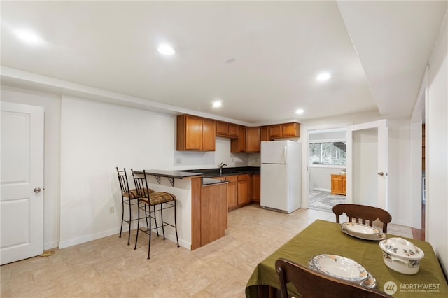 kitchen with dark countertops, a kitchen bar, brown cabinets, a peninsula, and freestanding refrigerator