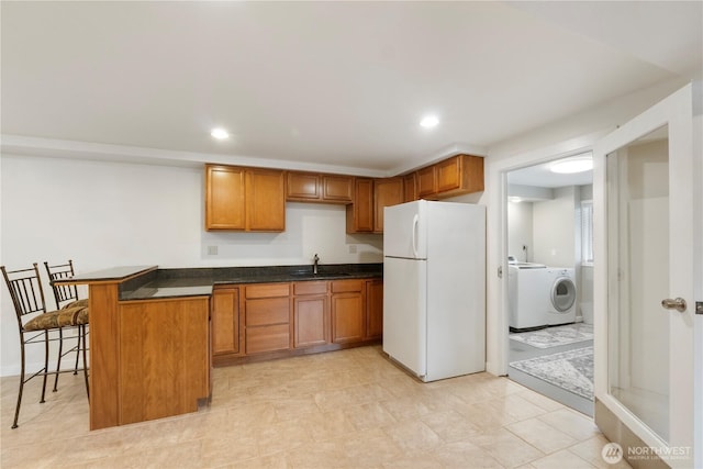 kitchen featuring washer / clothes dryer, freestanding refrigerator, a sink, a kitchen bar, and dark countertops