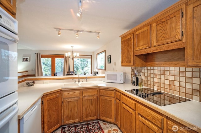 kitchen featuring a peninsula, white appliances, a sink, light countertops, and brown cabinets