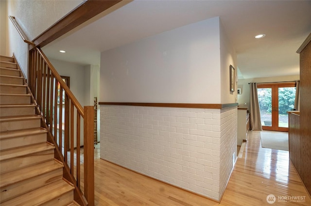 stairs featuring recessed lighting, a wainscoted wall, brick wall, wood finished floors, and french doors