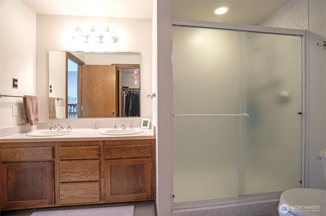 bathroom featuring a sink, a shower stall, toilet, and double vanity