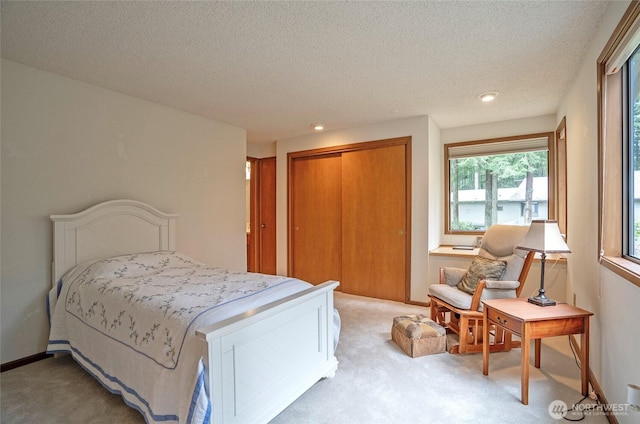 bedroom featuring a closet, light carpet, a textured ceiling, and baseboards