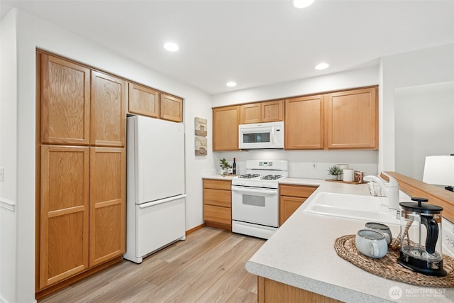 kitchen featuring white appliances, light countertops, light wood-type flooring, a sink, and recessed lighting