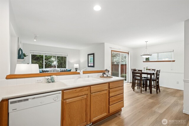 kitchen with white dishwasher, light wood-style flooring, a sink, light countertops, and pendant lighting