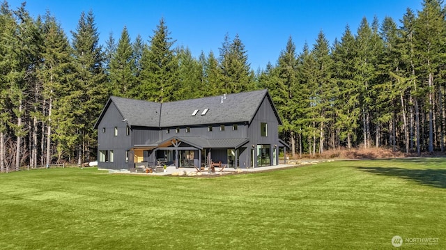 back of house featuring a patio area, a wooded view, and a yard