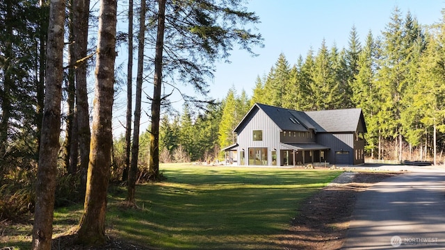 modern farmhouse style home with a garage, a front yard, driveway, and a forest view