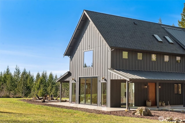 rear view of house featuring metal roof, a yard, roof with shingles, board and batten siding, and a standing seam roof