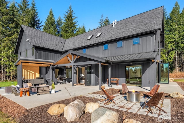 rear view of property with a standing seam roof, metal roof, board and batten siding, a patio area, and an outdoor living space with a fire pit