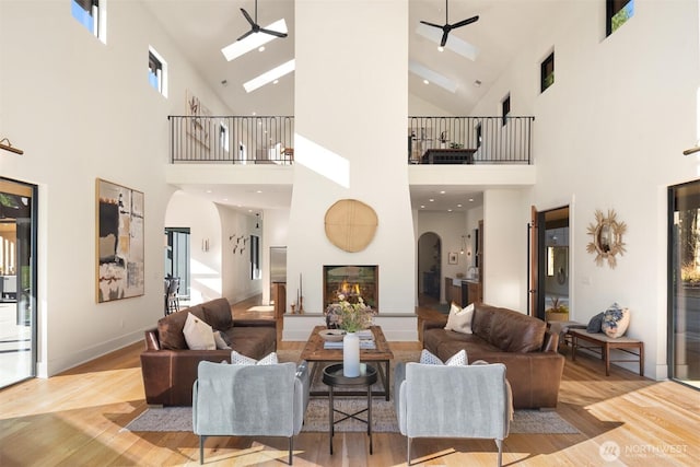 living room with ceiling fan, a lit fireplace, arched walkways, and wood finished floors