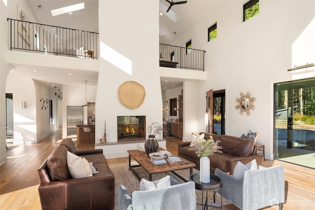 living area with a glass covered fireplace, a towering ceiling, recessed lighting, and wood finished floors