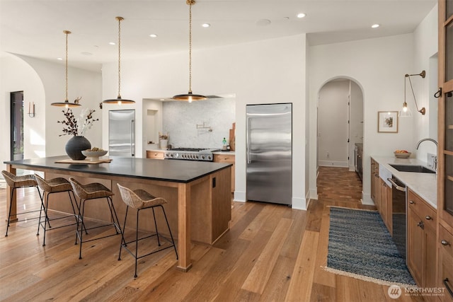 kitchen featuring arched walkways, stainless steel appliances, a sink, light wood-type flooring, and dark countertops