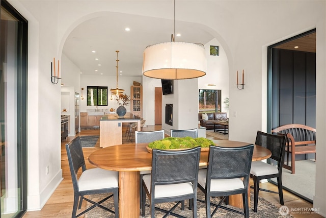 dining room featuring arched walkways, a large fireplace, recessed lighting, and light wood-style floors