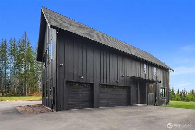 view of home's exterior featuring aphalt driveway, roof with shingles, central air condition unit, board and batten siding, and a garage