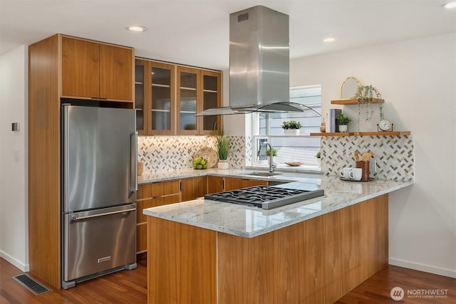 kitchen featuring visible vents, brown cabinets, freestanding refrigerator, a peninsula, and island exhaust hood