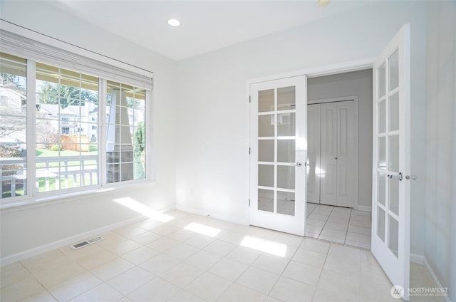 tiled empty room featuring plenty of natural light, visible vents, baseboards, and french doors