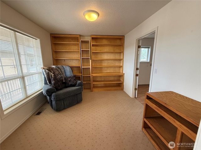 living area featuring light colored carpet, visible vents, a textured ceiling, and baseboards