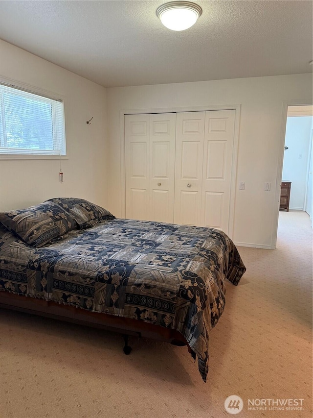 carpeted bedroom featuring a textured ceiling, baseboards, and a closet