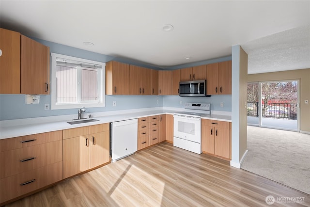 kitchen with white appliances, light countertops, light wood-type flooring, and a sink