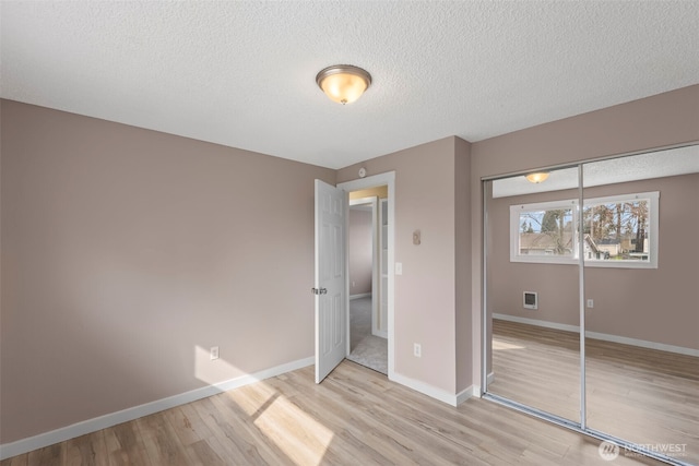 unfurnished bedroom featuring visible vents, a textured ceiling, a closet, light wood-style floors, and baseboards