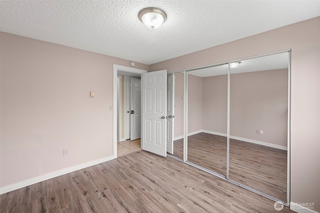 unfurnished bedroom featuring wood finished floors, baseboards, a closet, and a textured ceiling