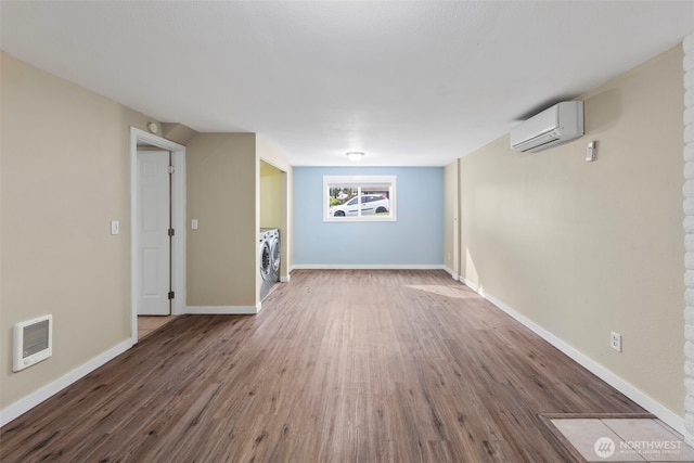 unfurnished living room featuring washing machine and clothes dryer, baseboards, a wall unit AC, and wood finished floors