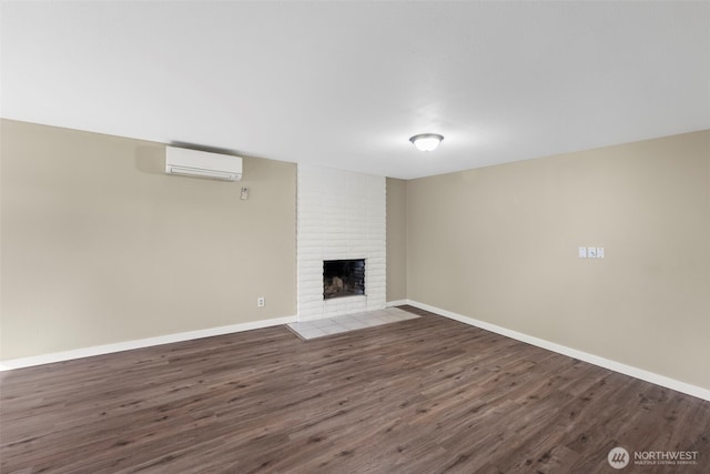 unfurnished living room with a brick fireplace, a wall mounted air conditioner, baseboards, and wood finished floors