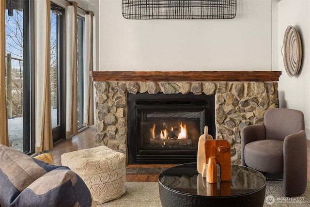 living area featuring a wealth of natural light, a stone fireplace, and wood finished floors