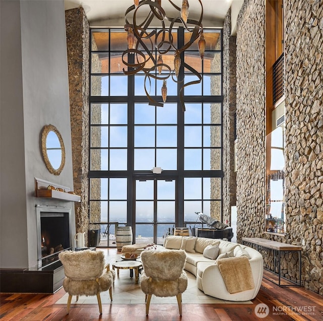 living room with a notable chandelier, wood finished floors, a towering ceiling, a lit fireplace, and plenty of natural light