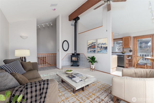 living room with a ceiling fan, a wood stove, beam ceiling, high vaulted ceiling, and track lighting