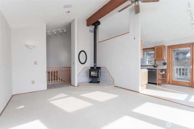 unfurnished living room with beamed ceiling, rail lighting, a wood stove, and light colored carpet