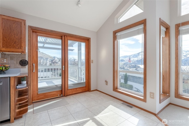 doorway to outside featuring lofted ceiling, visible vents, baseboards, and light tile patterned floors