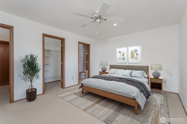 bedroom featuring baseboards, ensuite bath, a walk in closet, and light colored carpet