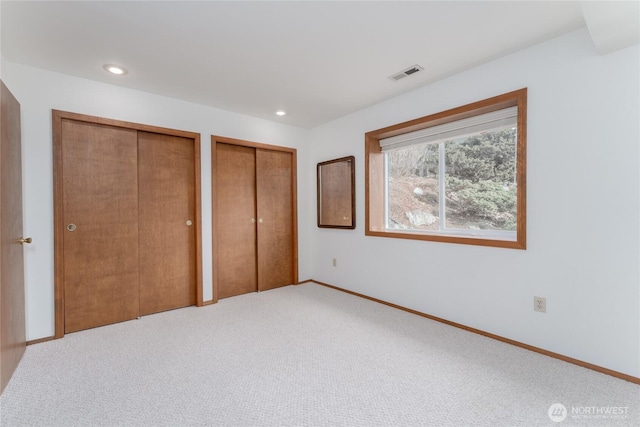 unfurnished bedroom with baseboards, carpet, visible vents, and two closets