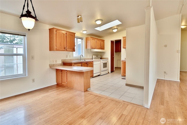 kitchen with a sink, white appliances, a peninsula, a skylight, and light countertops