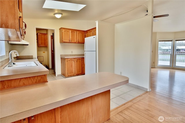 kitchen featuring light wood finished floors, light countertops, a skylight, freestanding refrigerator, and a sink