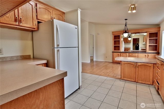 kitchen featuring baseboards, lofted ceiling, light tile patterned flooring, freestanding refrigerator, and decorative light fixtures