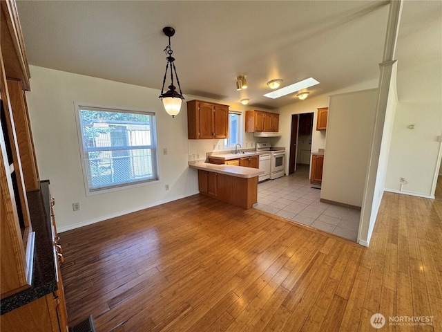 kitchen with range, light countertops, a peninsula, brown cabinets, and light wood-style floors