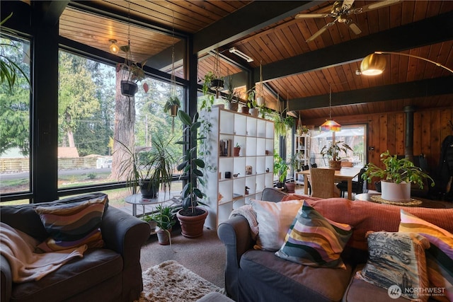 sunroom with beamed ceiling, wooden ceiling, a wood stove, and a ceiling fan