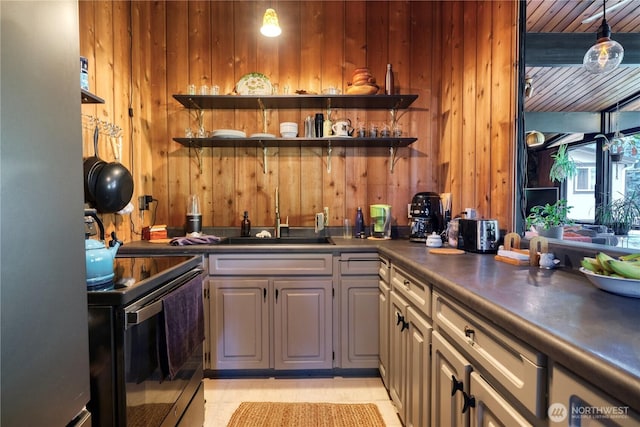 kitchen with a sink, open shelves, dark countertops, stainless steel appliances, and wooden walls