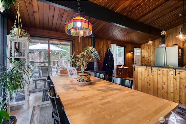 dining space featuring a wealth of natural light, beam ceiling, wooden walls, and wooden ceiling