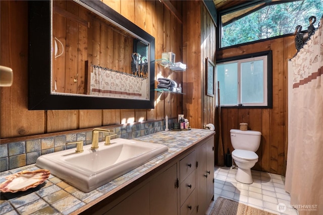 full bath with vanity, wooden walls, toilet, and a wealth of natural light