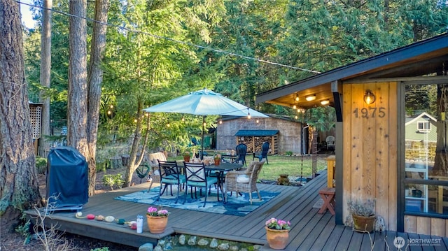 wooden terrace with outdoor dining space, a grill, and an outdoor structure