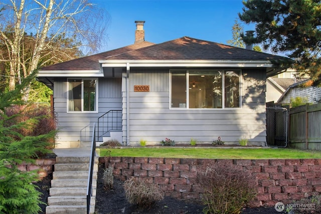 exterior space featuring roof with shingles, fence, and a chimney