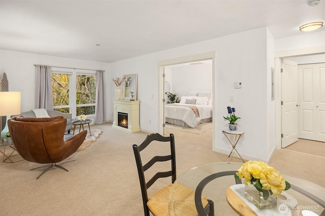 living area with a lit fireplace, baseboards, and light colored carpet